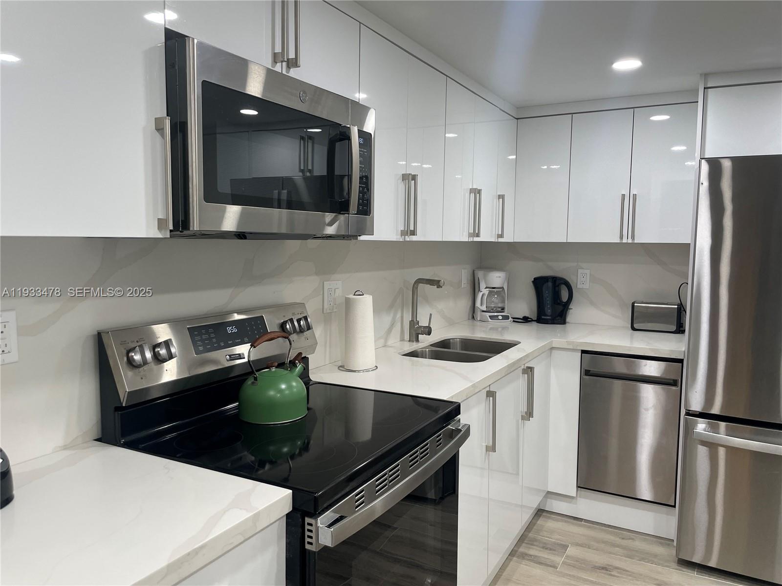 A modern kitchen features white glossy cabinets, stainless steel appliances, and white marble-patterned countertops — 2030 S Ocean Dr # 805, Hallandale Beach FL 33009, HALLANDALE BEACH, FL