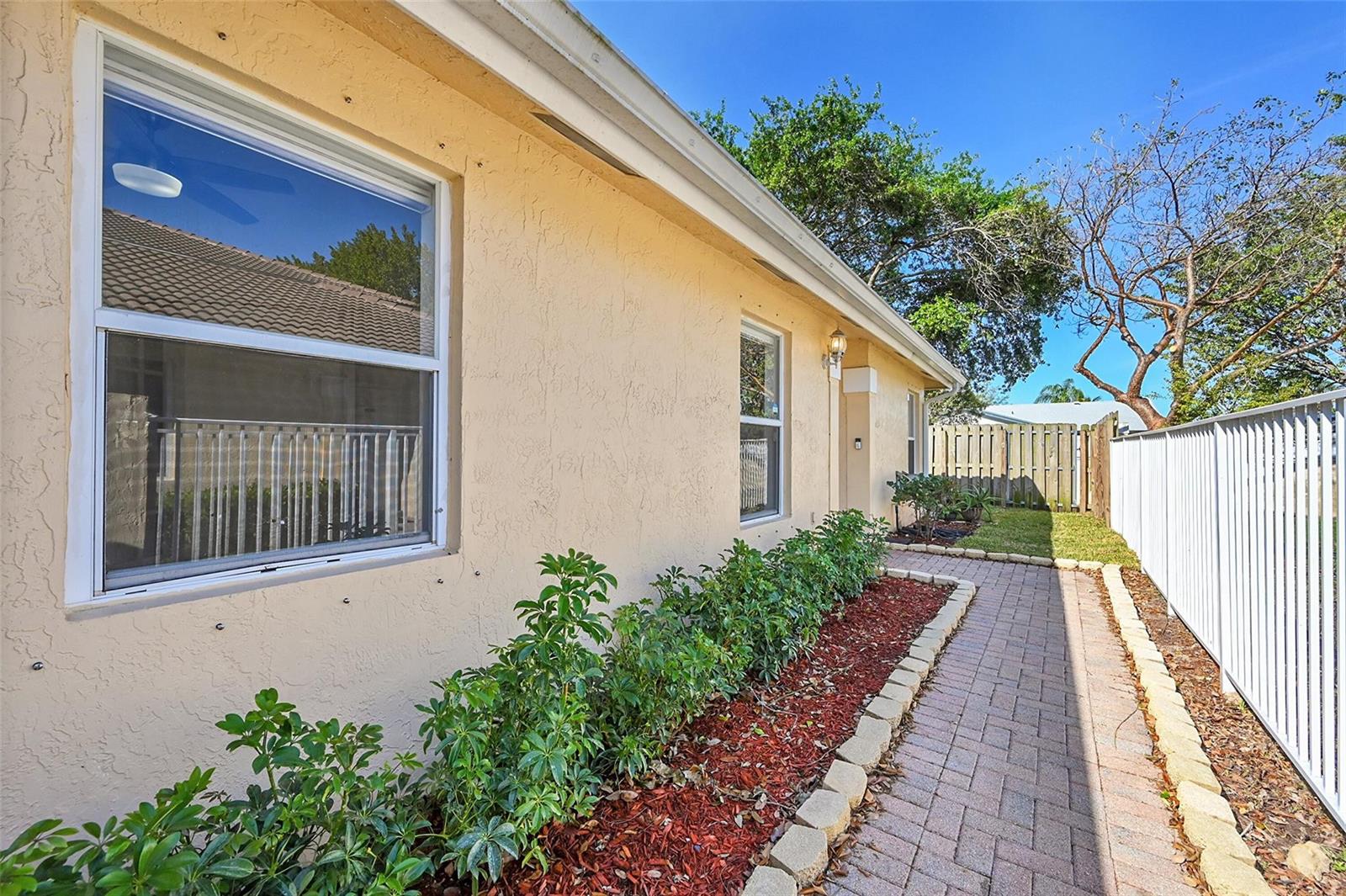 A paved walkway runs alongside a stucco house with a garden bed and white fence — 5361 NW 90th Avenue, Sunrise FL 33351, SUNRISE, FL