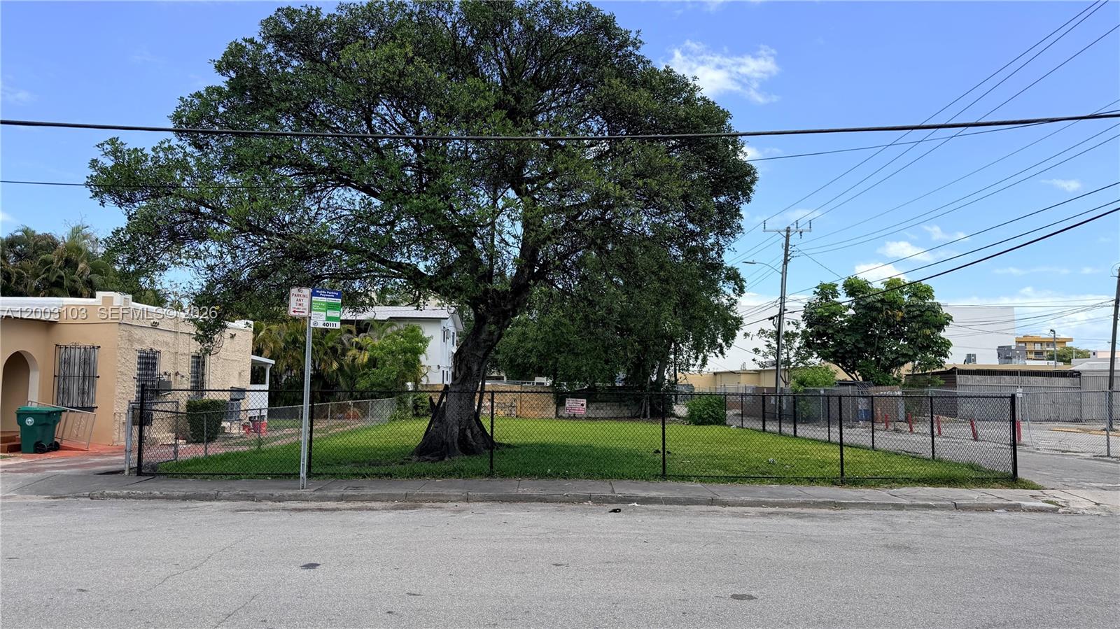 A fenced, grassy vacant lot features a large mature tree under a blue sky — 33 NW 21st Ave, Miami FL 33125, MIAMI, FL