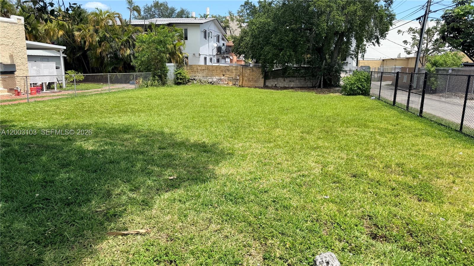 A grassy, fenced-in backyard lot sits adjacent to a white building and a paved road — 33 NW 21st Ave, Miami FL 33125, MIAMI, FL