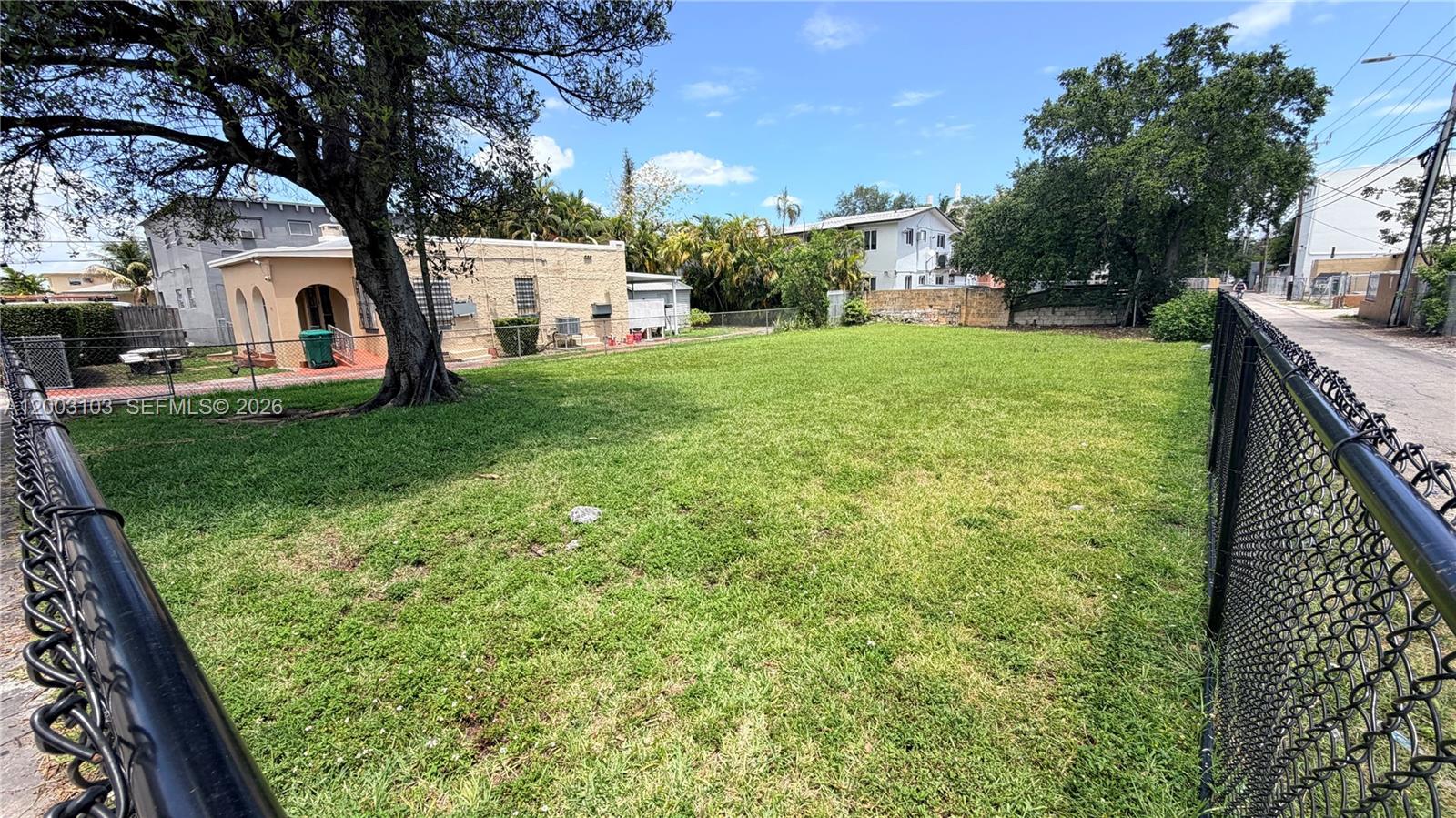 A large, grassy vacant lot is enclosed by a chain-link fence next to a house — 33 NW 21st Ave, Miami FL 33125, MIAMI, FL