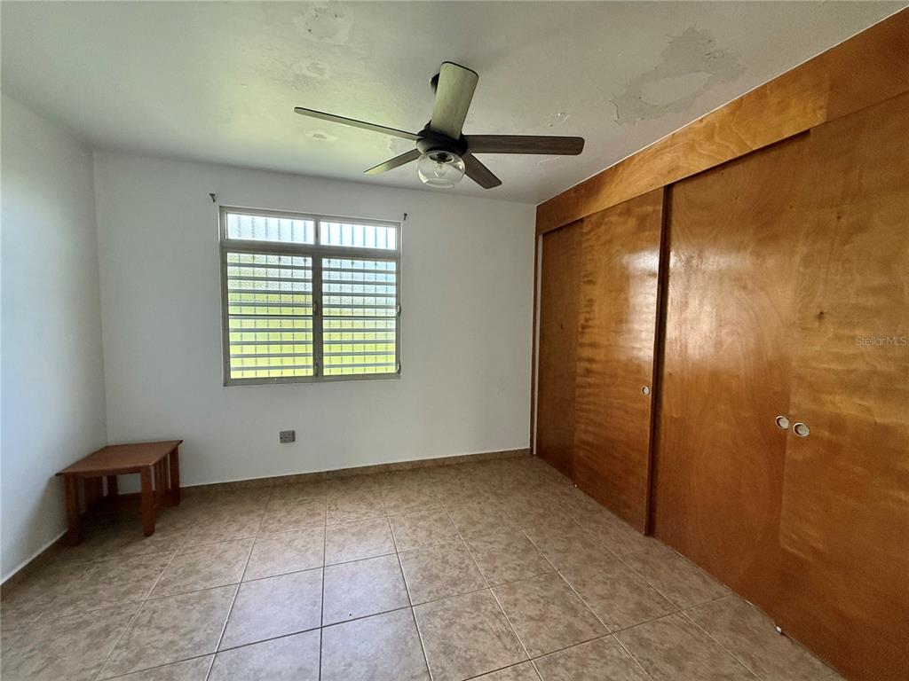 A bedroom features light tile flooring, a ceiling fan, a window, and wooden sliding closets — Carr 411 km 0.20 BO. CALVACHE, RINCON, PR