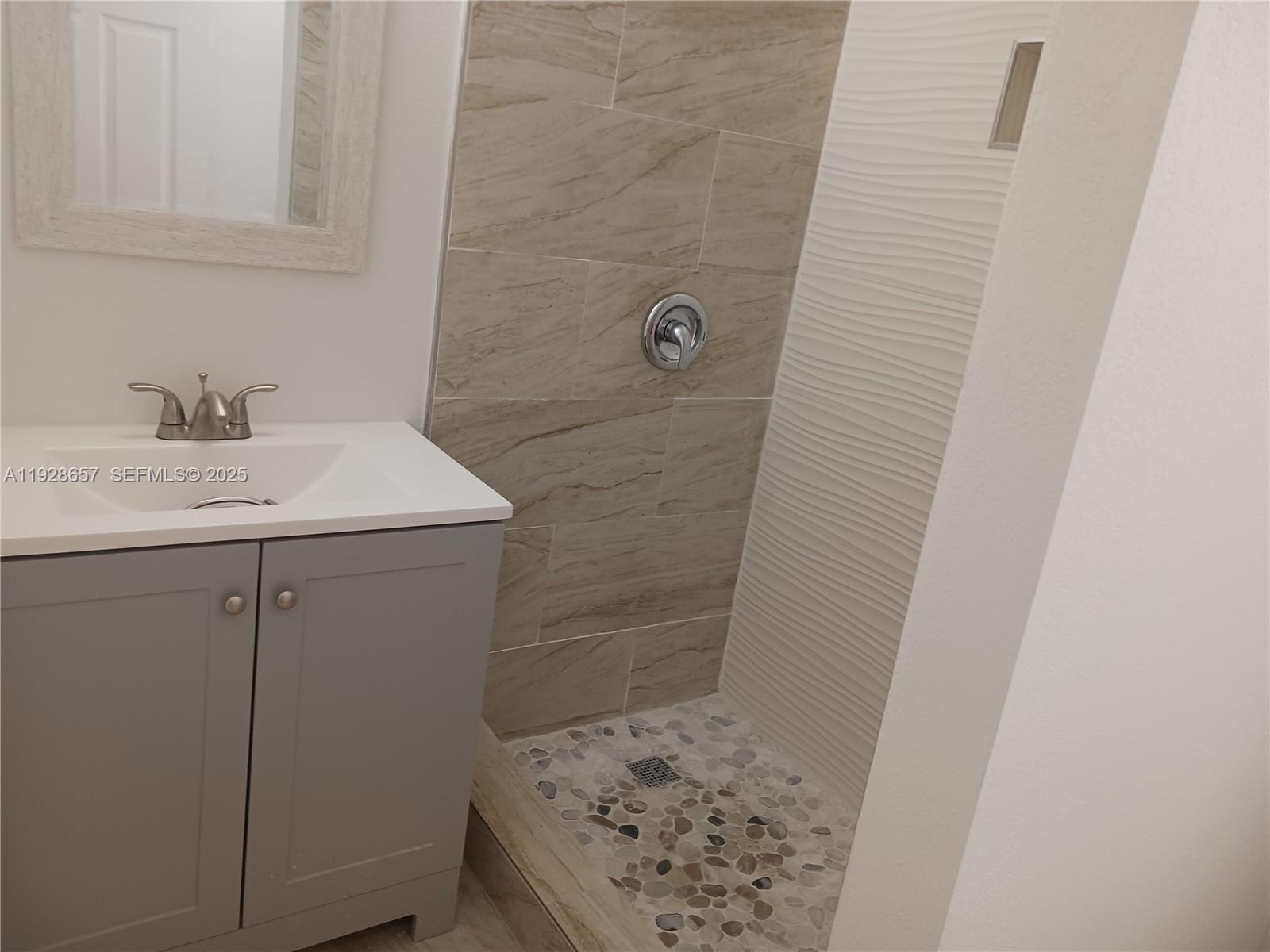A bathroom features a gray vanity, a mirror, and a walk-in shower with stone flooring — 650 SW 44th Ct, Miami FL 33134, MIAMI, FL