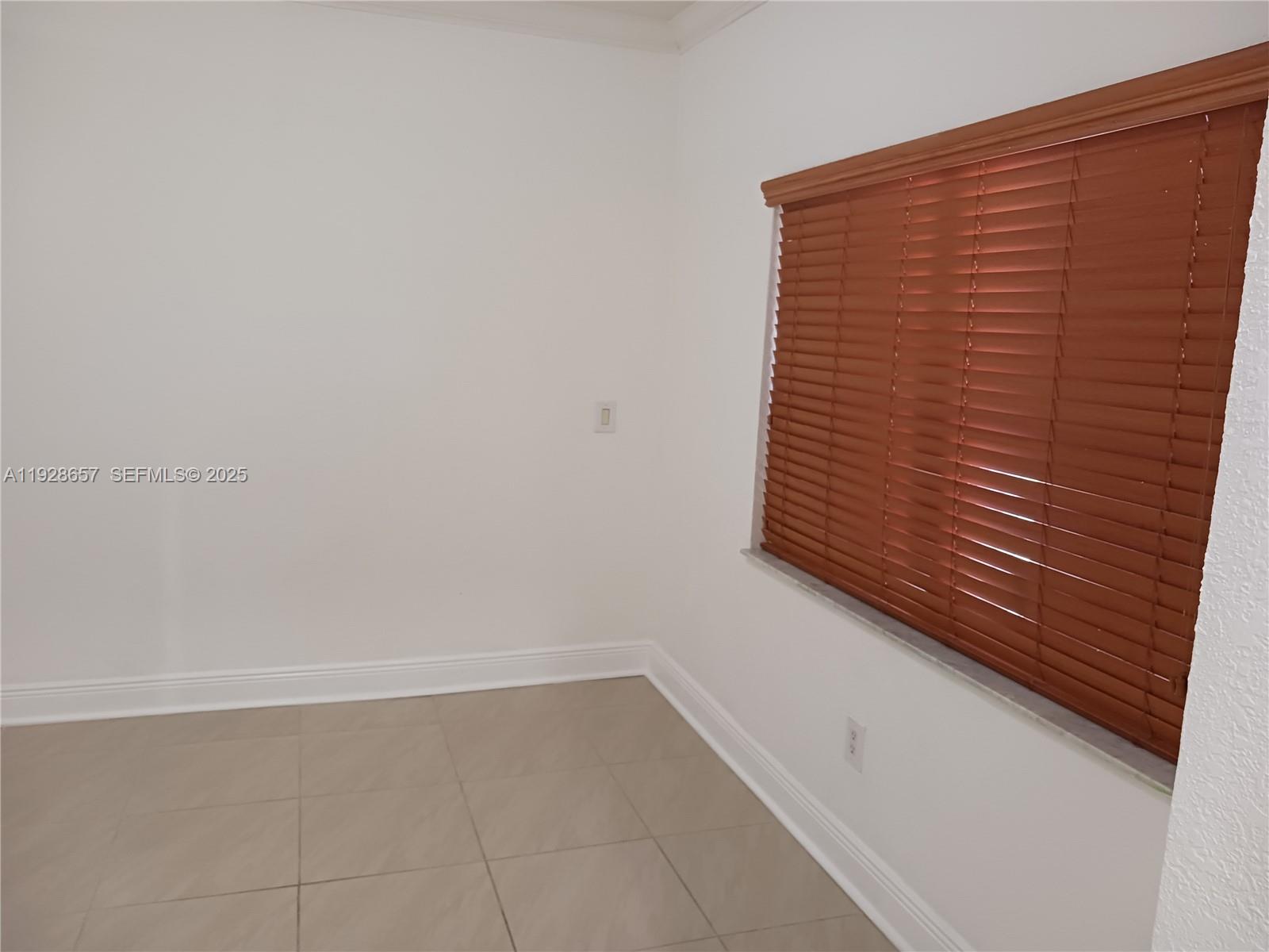 An empty room features white walls, light-colored tile flooring, and a window with wood blinds — 650 SW 44th Ct, Miami FL 33134, MIAMI, FL