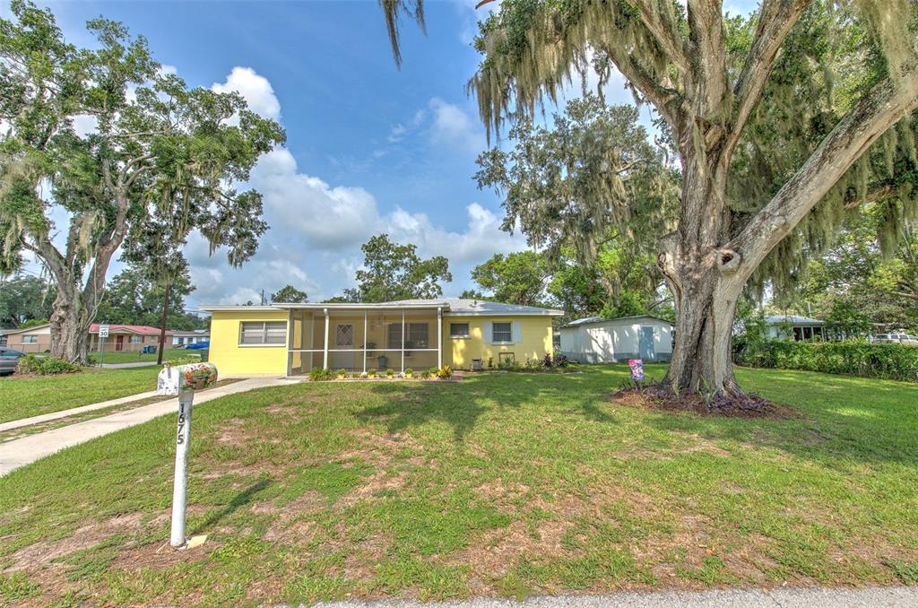 A yellow single-story house with a screened front porch sits on a grassy lot with trees — 1675 N TATE AVENUE, BARTOW, FL