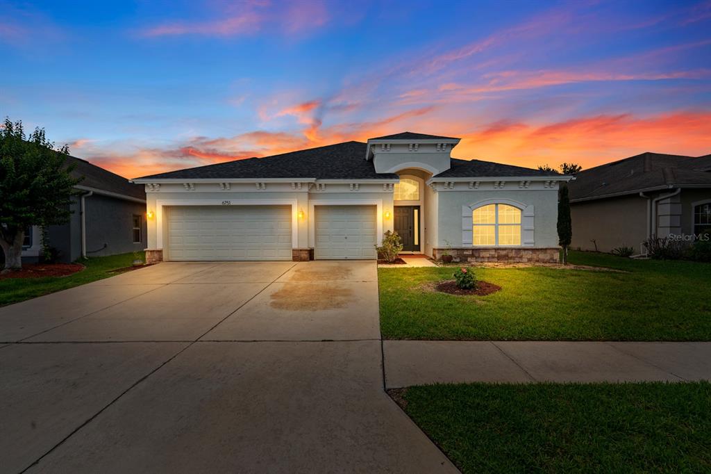 A single-story house with a three-car garage and a concrete driveway under a blue sky — 6751 BOULDER RUN LOOP, WESLEY CHAPEL, FL