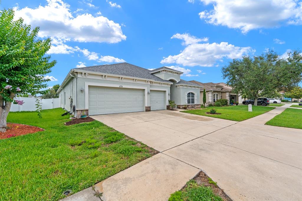 A grassy backyard features a white vinyl fence, a small tree, and a pond view — 6751 BOULDER RUN LOOP, WESLEY CHAPEL, FL