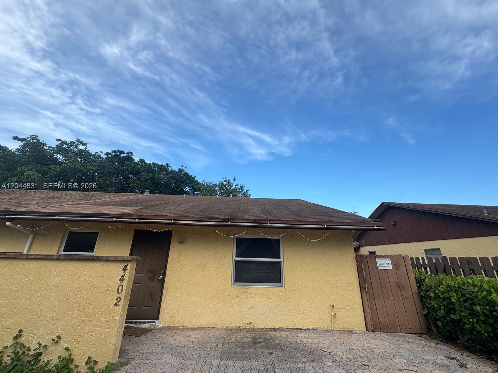 A yellow single-story house features a brown door, a paved driveway, and a wooden fence — 4402 NW 5th Ave # 4402, Deerfield Beach FL 33064, DEERFIELD BEACH, FL