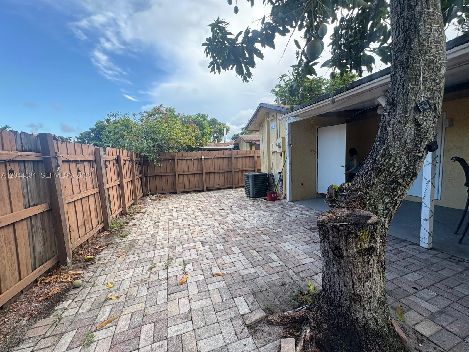 A backyard patio features brick pavers, a wooden fence, and a large tree — 4402 NW 5th Ave # 4402, Deerfield Beach FL 33064, DEERFIELD BEACH, FL
