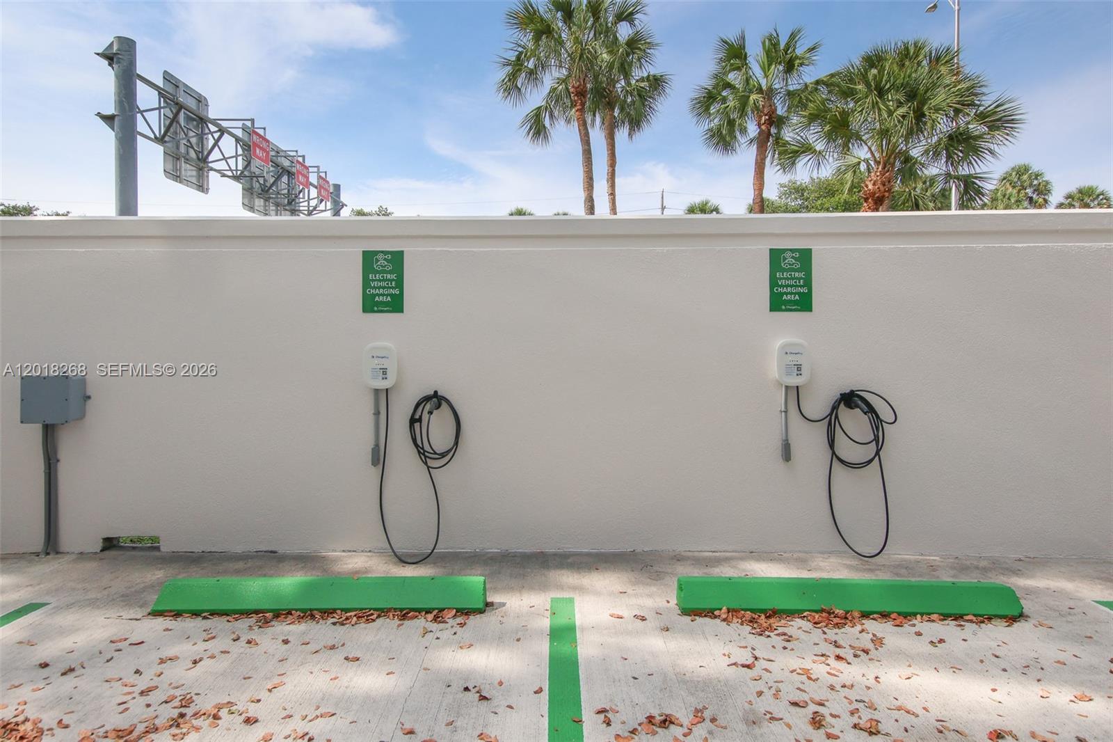 Two electric vehicle charging stations are mounted on a white wall above green parking bumpers — 1900 Glades Rd # 353, Boca Raton FL 33431, BOCA RATON, FL