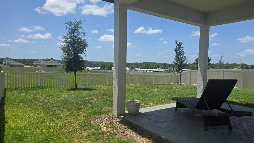 A covered concrete patio overlooks a grassy backyard enclosed by a white vinyl fence — 12163 STIRRUP DRIVE, DADE CITY, FL