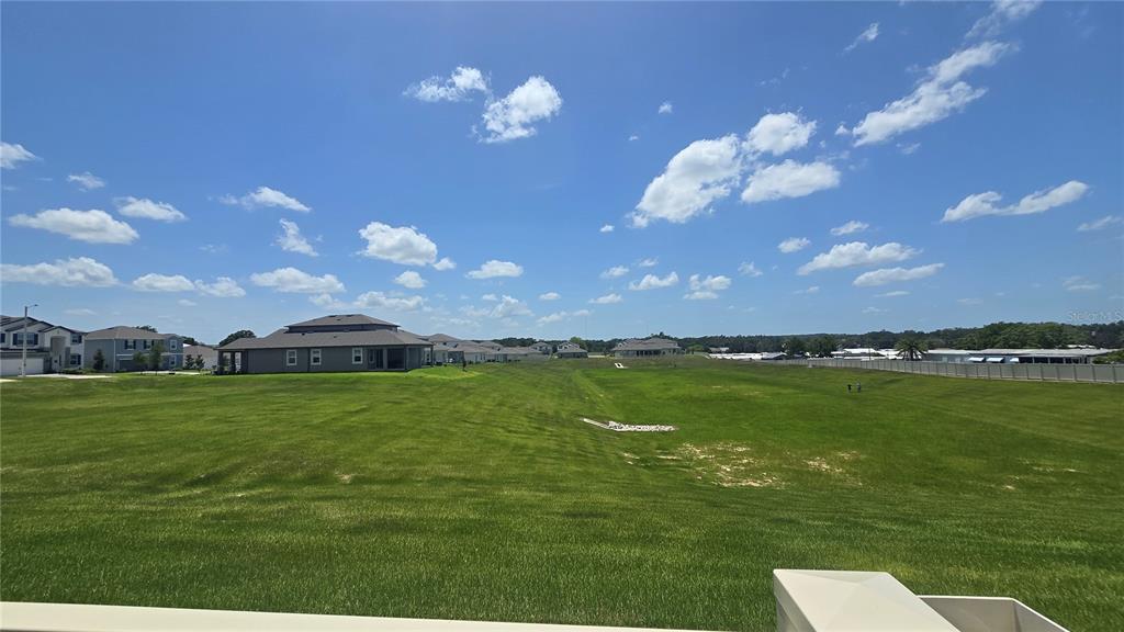 A wide, grassy field sits in front of several suburban houses under a blue sky — 12163 STIRRUP DRIVE, DADE CITY, FL