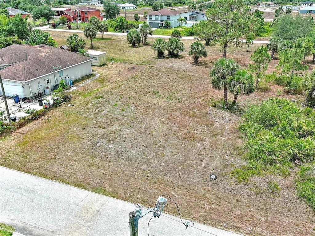 An aerial view shows a vacant, grassy residential lot next to a single-story house — 914 MERCURY AVENUE S, LEHIGH ACRES, FL