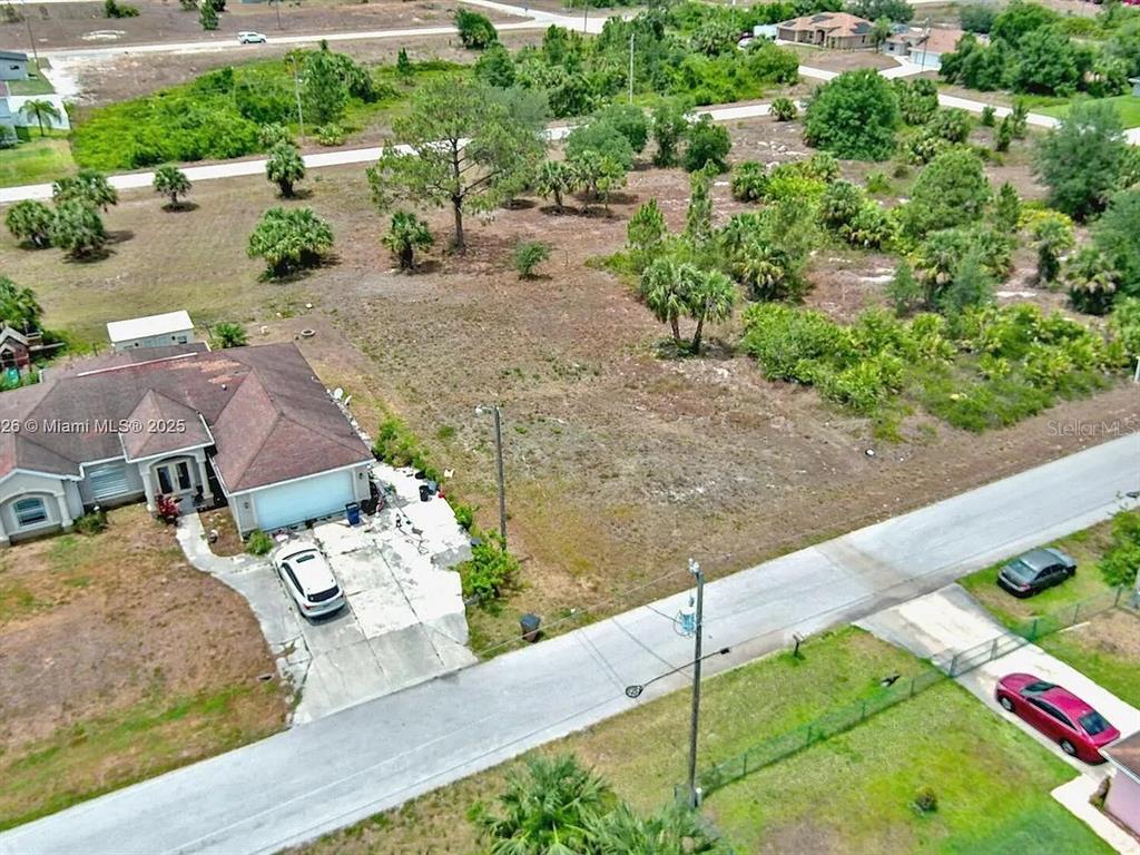 An aerial view shows a residential house with a driveway next to a vacant lot — 914 MERCURY AVENUE S, LEHIGH ACRES, FL
