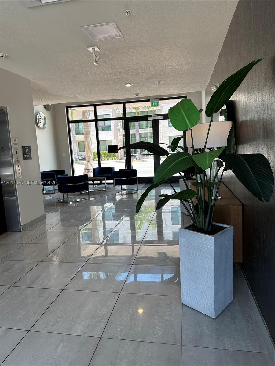 A modern building lobby features large windows, tiled floors, blue chairs, and a potted plant — 8201 NW 41st St # 203, Doral FL 33166, DORAL, FL
