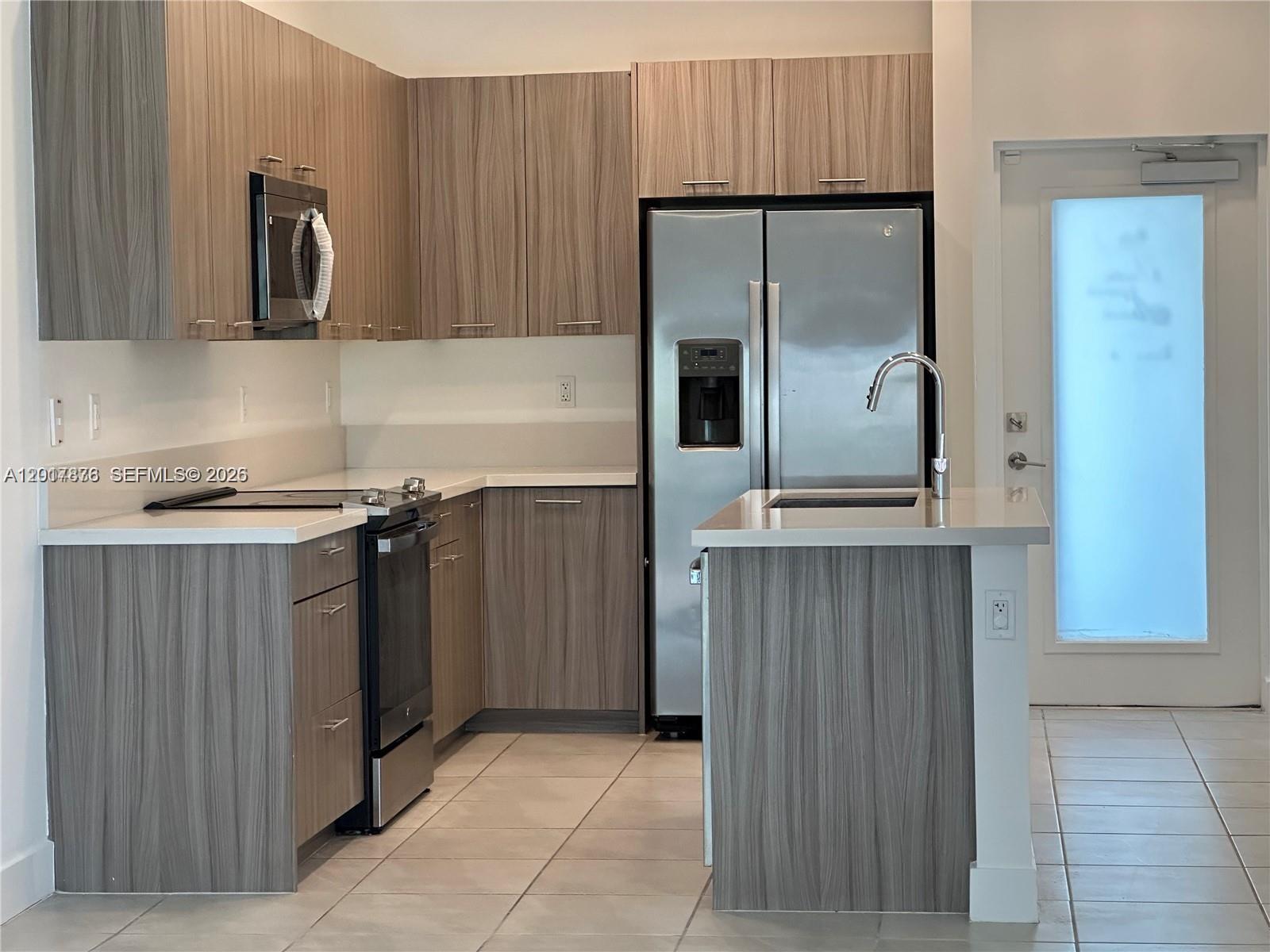 A modern kitchen features wood-grain cabinets, stainless steel appliances, and a small island with sink — 8201 NW 41st St # 203, Doral FL 33166, DORAL, FL