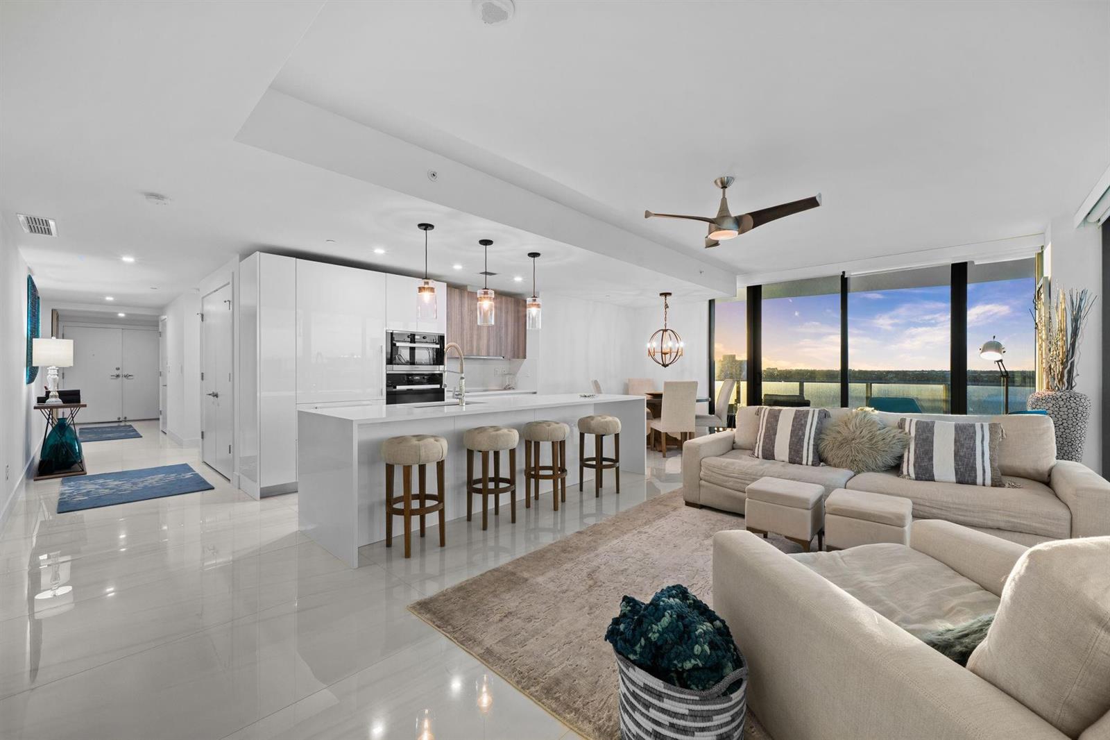 An open-concept living area features a modern white kitchen, island seating, and floor-to-ceiling windows — 730 N Ocean Boulevard # 701, Pompano Beach FL 33062, POMPANO BEACH, FL