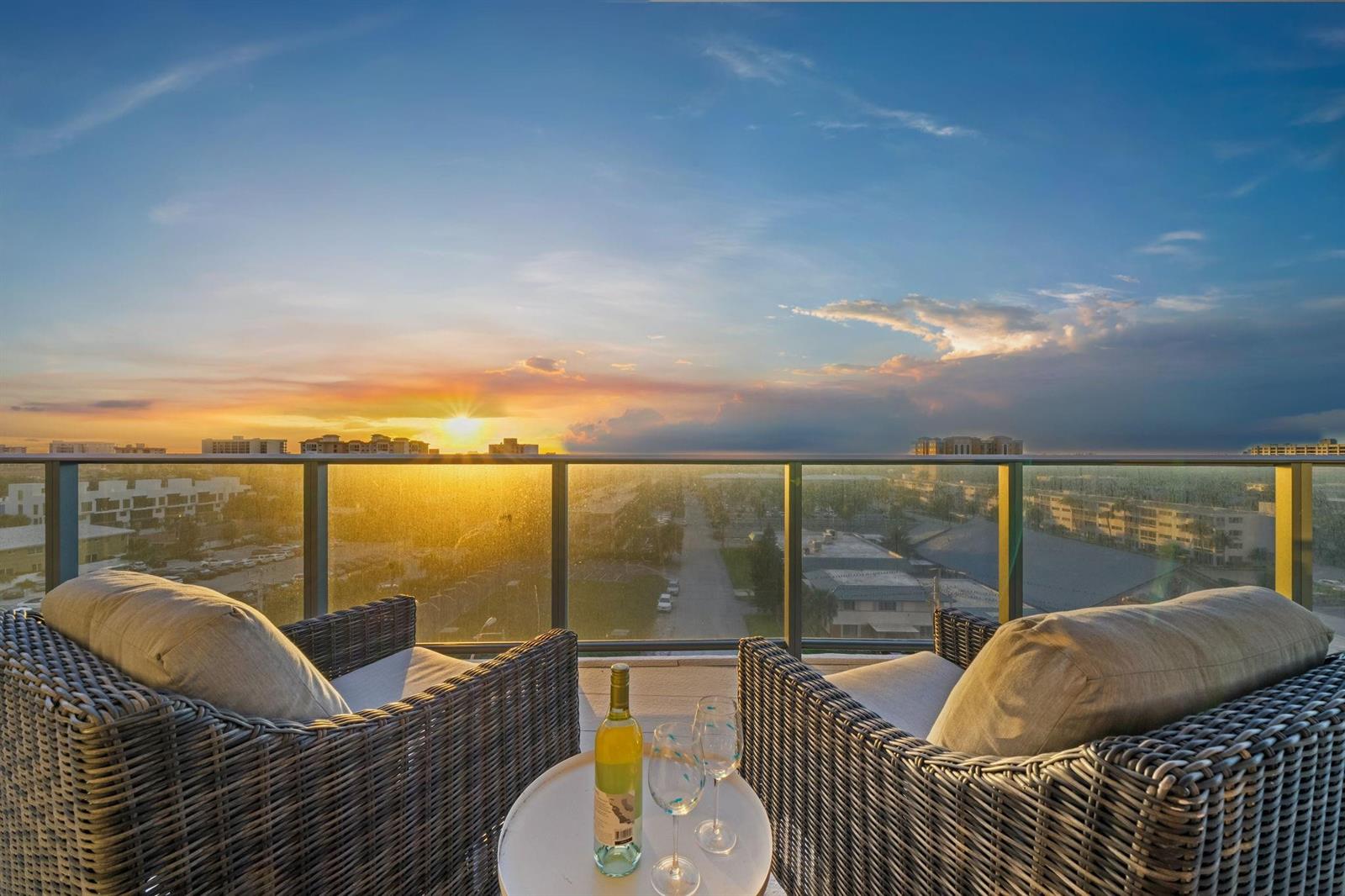 Two wicker chairs and a wine set sit on a balcony overlooking a sunset view — 730 N Ocean Boulevard # 701, Pompano Beach FL 33062, POMPANO BEACH, FL