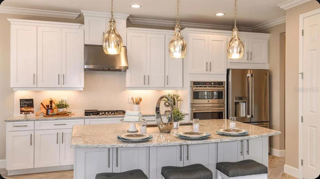 A modern kitchen features white cabinetry, a granite-topped island, stainless steel appliances, and pendant lighting — 35709 EMBERVIEW DRIVE, ZEPHYRHILLS, FL