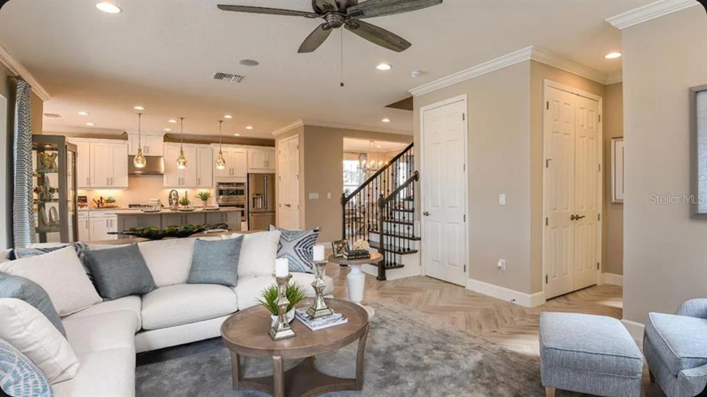 An open-concept living room with a white sectional sofa, round coffee table, and adjacent kitchen — 35709 EMBERVIEW DRIVE, ZEPHYRHILLS, FL