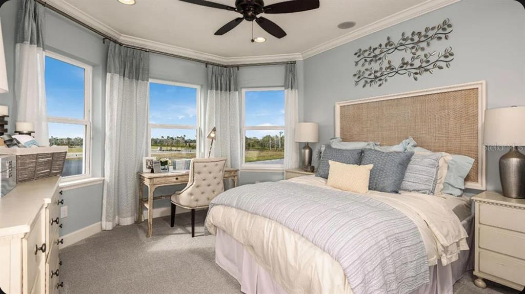 A bedroom features a bed with a woven headboard, a desk, and windows overlooking water — 35709 EMBERVIEW DRIVE, ZEPHYRHILLS, FL