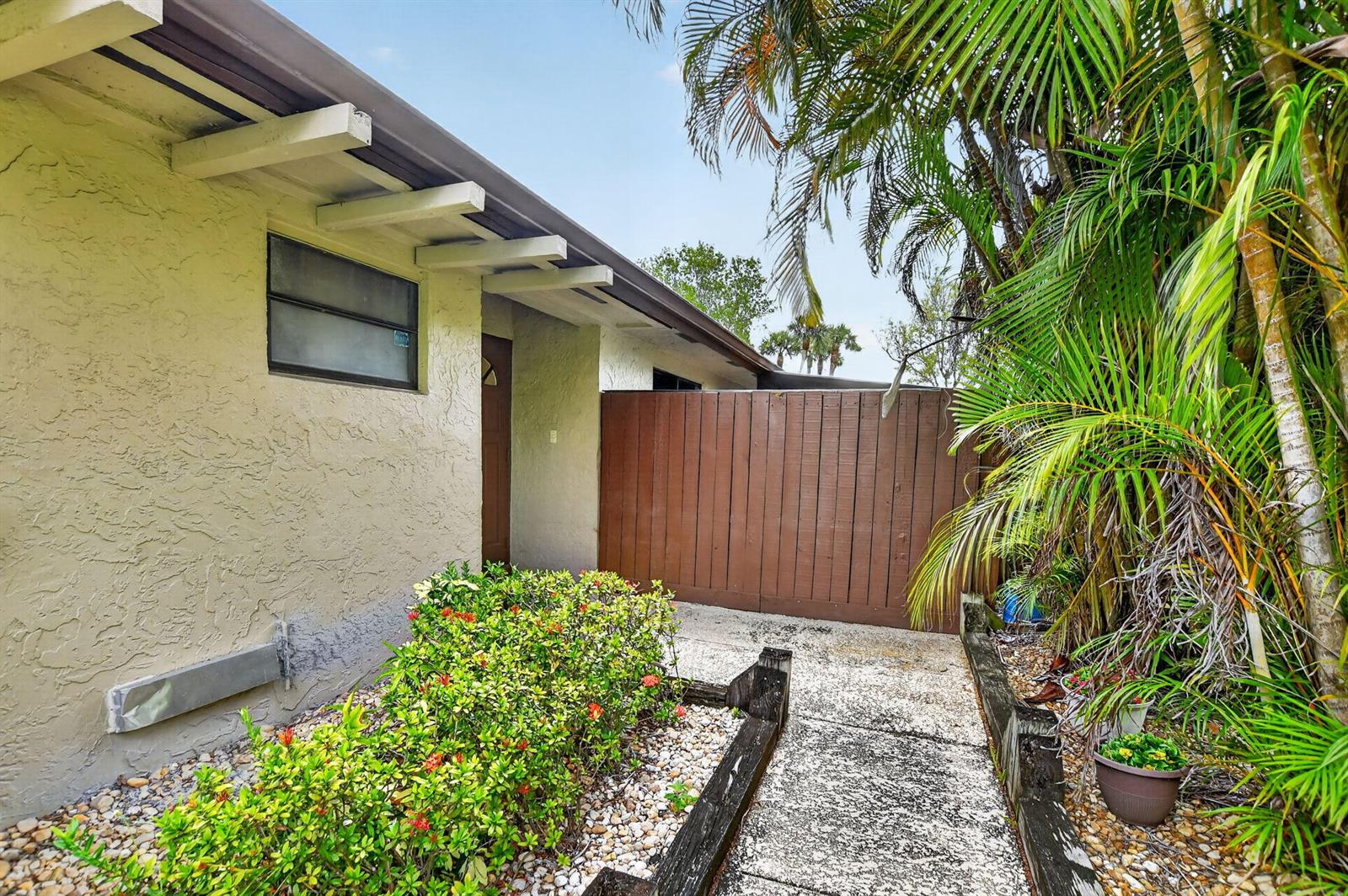 A walkway leads past a garden bed and palm trees toward a wooden privacy fence — 22718 Vistawood Way, Boca Raton FL 33428, BOCA RATON, FL