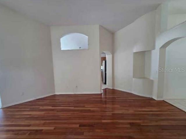 An empty room with hardwood floors, a recessed wall niche, and an arched entryway — 12533 SPARKLEBERRY ROAD, TAMPA, FL