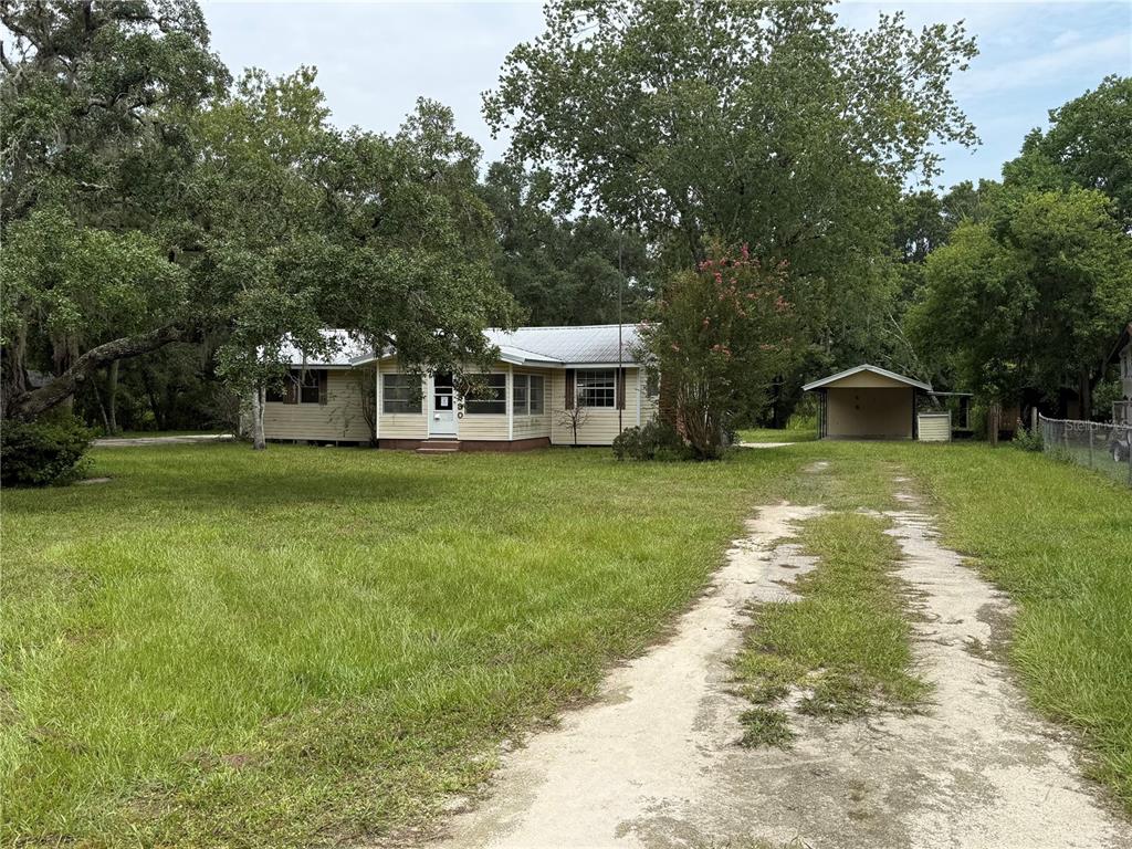 A single-story house with light siding and a metal roof sits behind a dirt driveway — 4830 SW 123RD ROAD, WEBSTER, FL