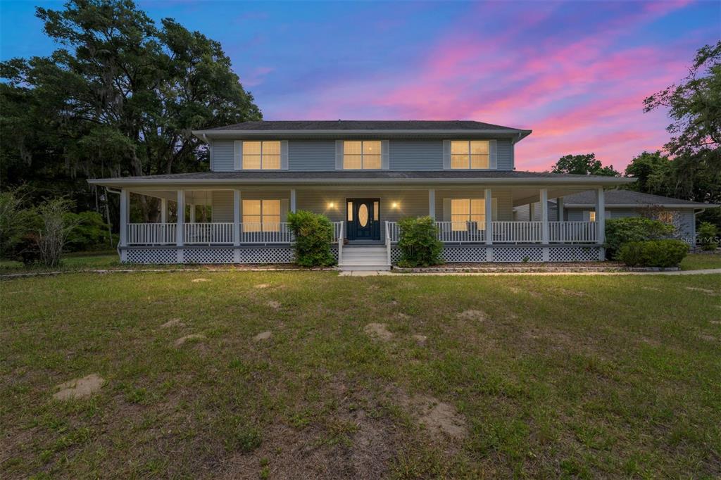 A two-story house with a full-length front porch sits on a grassy lawn at dusk — 15725 SE 36TH AVENUE, SUMMERFIELD, FL