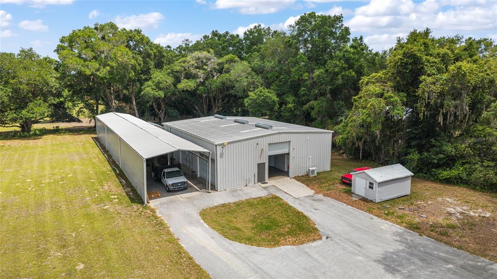 An aerial view shows a metal warehouse building with an attached carport and small shed — 15725 SE 36TH AVENUE, SUMMERFIELD, FL