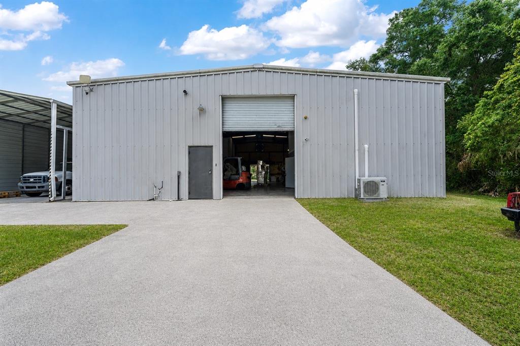 A metal warehouse building features a roll-up door, a pedestrian door, and a concrete driveway — 15725 SE 36TH AVENUE, SUMMERFIELD, FL