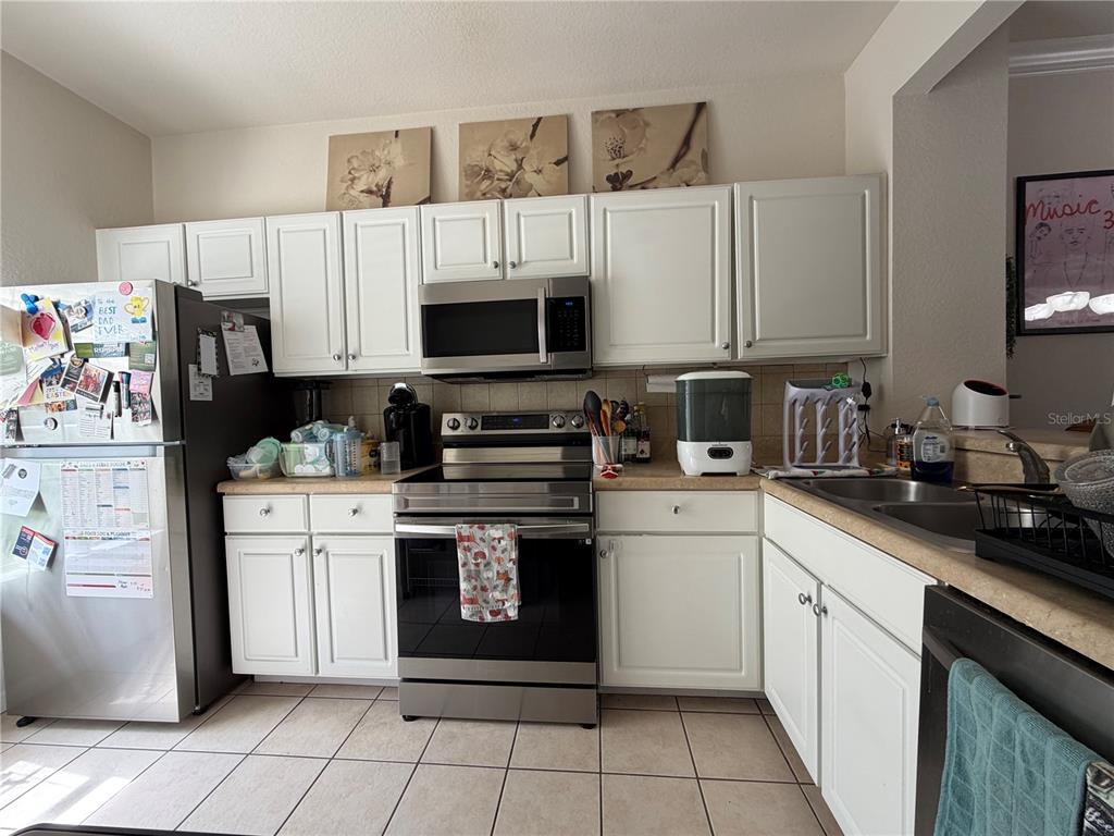 A kitchen features white cabinets, stainless steel appliances, and light-colored countertops — 4445 NW 49TH STREET UNIT 102, GAINESVILLE, FL