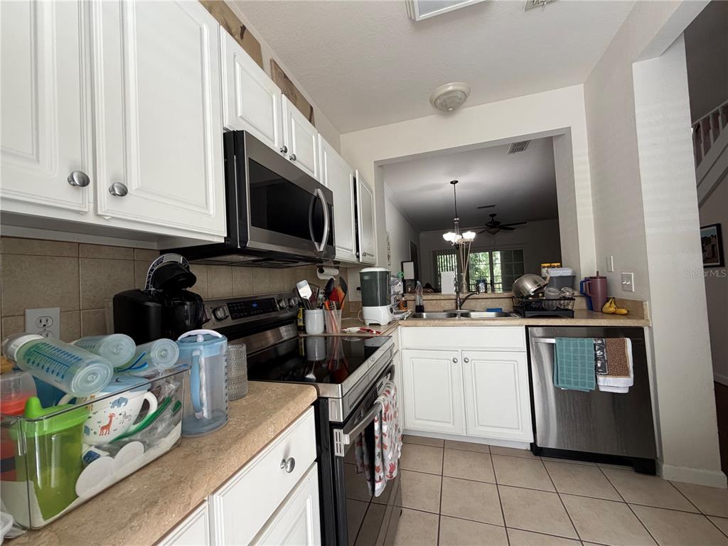A kitchen features white cabinets, stainless steel appliances, tile flooring, and a pass-through window — 4445 NW 49TH STREET UNIT 102, GAINESVILLE, FL
