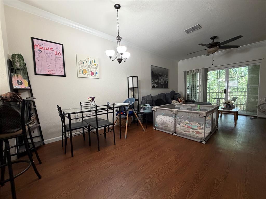 A dining area and living room with wood-look flooring, a glass table, and a playpen — 4445 NW 49TH STREET UNIT 102, GAINESVILLE, FL