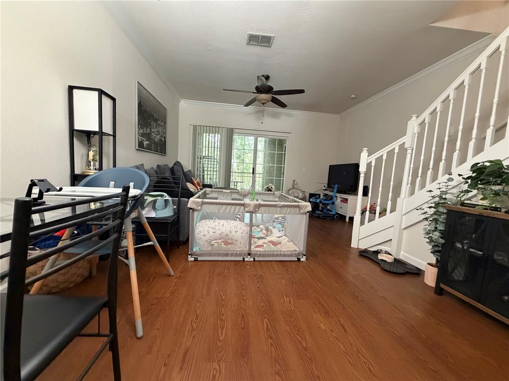 A living room with wood-look flooring, a playpen, and a staircase with white railings — 4445 NW 49TH STREET UNIT 102, GAINESVILLE, FL