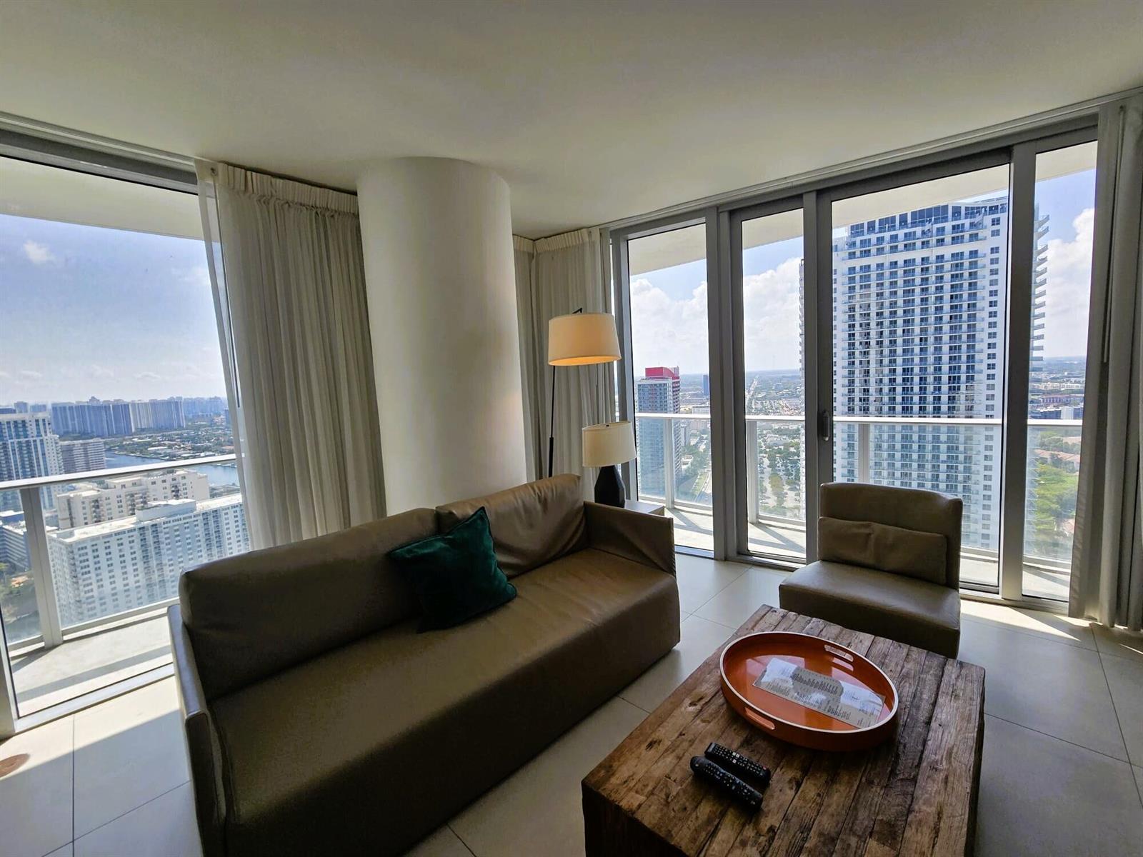 A modern living room features a leather sofa, wood coffee table, and floor-to-ceiling city views — 4111 S Ocean Drive # 3011, Hollywood FL 33019, HOLLYWOOD, FL