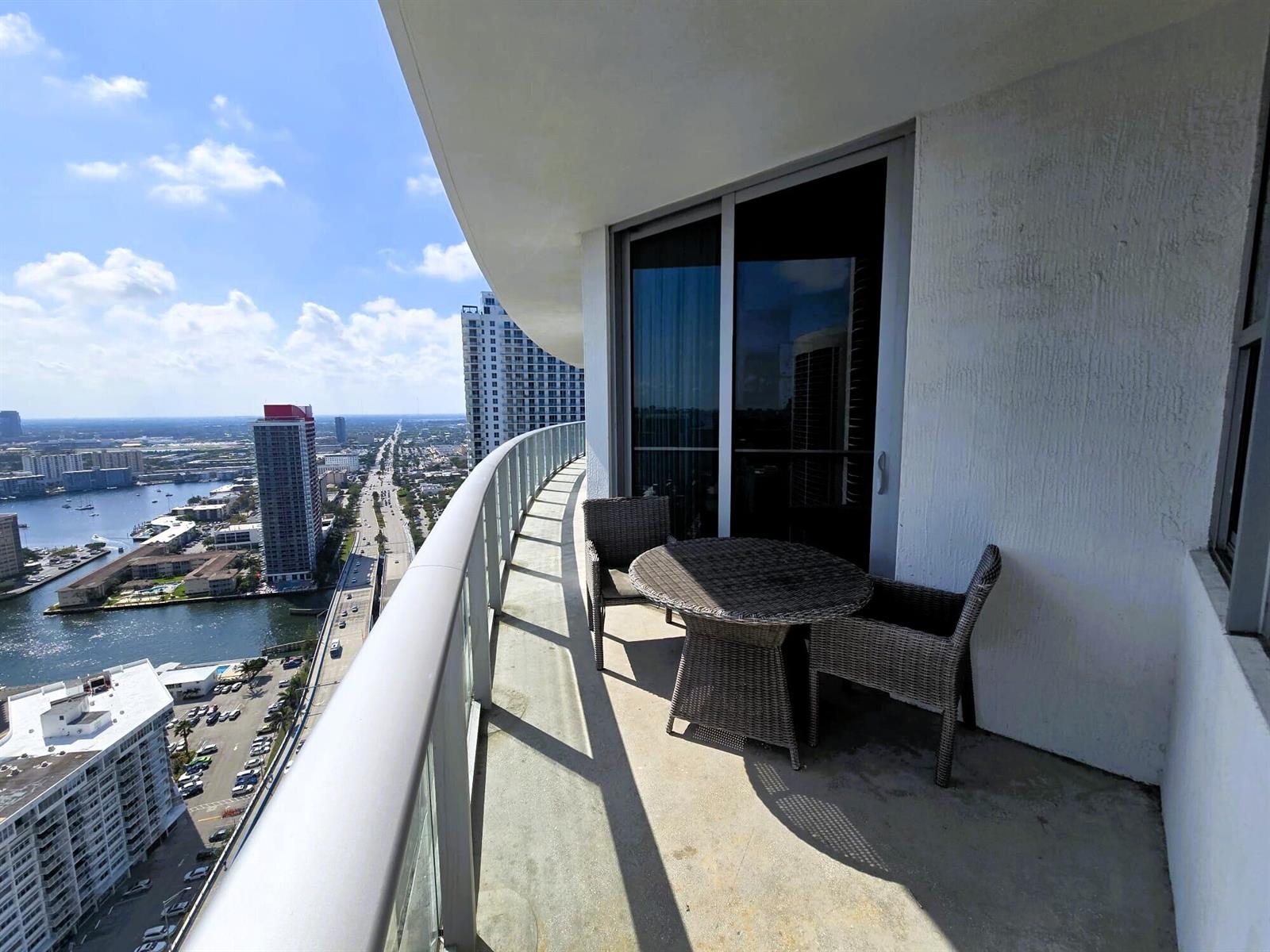 A high-rise balcony features a small wicker table and two chairs overlooking a city skyline — 4111 S Ocean Drive # 3011, Hollywood FL 33019, HOLLYWOOD, FL