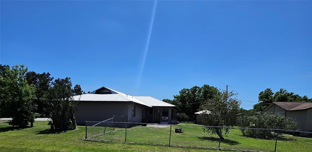 A view of the rear exterior of a house with a metal roof and yard — 3481 NE MASTERS AVENUE, ARCADIA, FL