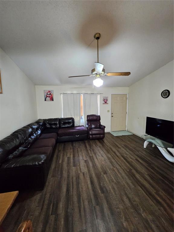 A living room features dark wood-look flooring, a large sectional sofa, and a ceiling fan — 3481 NE MASTERS AVENUE, ARCADIA, FL