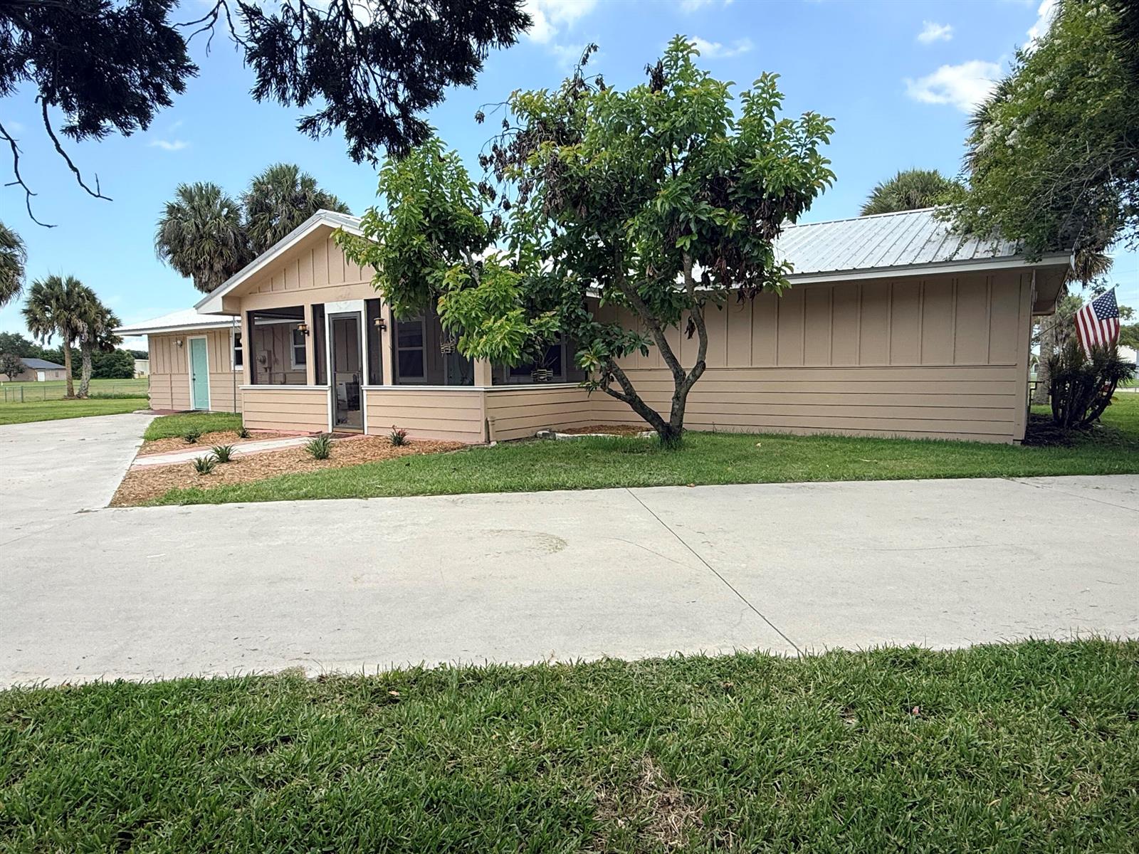 A tan, single-story house with a metal roof, screened porch, and a large concrete driveway — 13605 SW 144th Parkway, Okeechobee FL 34974, OKEECHOBEE, FL