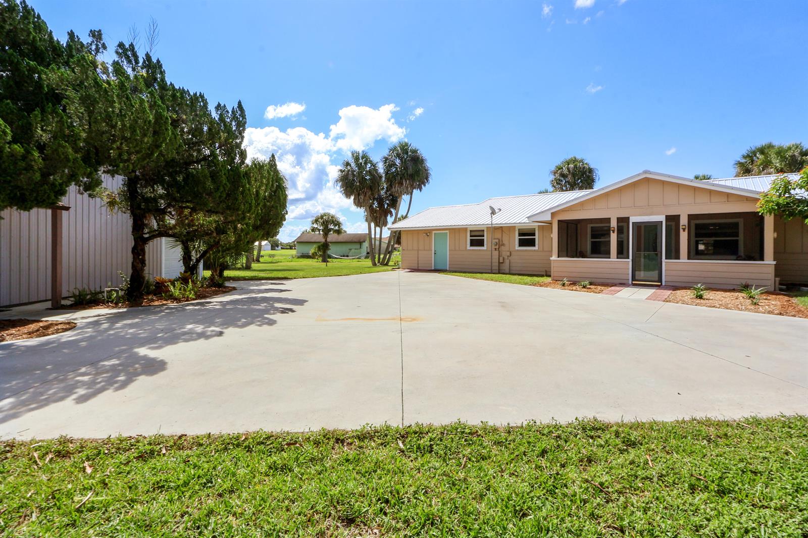 A wide concrete driveway leads to a tan house with a screened-in porch and palm trees — 13605 SW 144th Parkway, Okeechobee FL 34974, OKEECHOBEE, FL