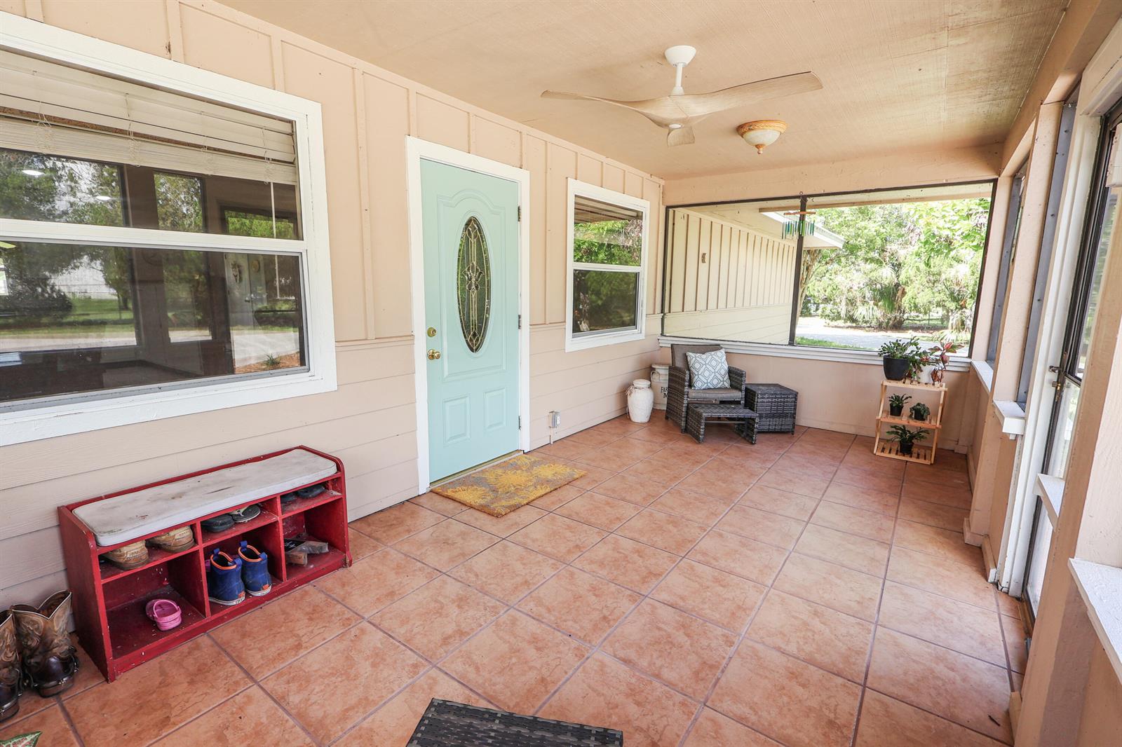A covered porch features a light blue front door, tiled flooring, and a red shoe rack — 13605 SW 144th Parkway, Okeechobee FL 34974, OKEECHOBEE, FL