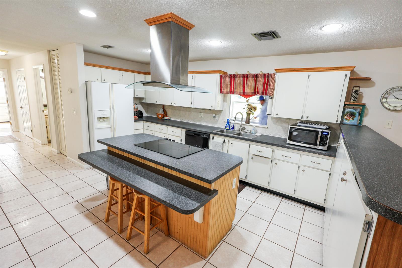 A kitchen features white cabinets, a dark countertop island with a cooktop, and tile flooring — 13605 SW 144th Parkway, Okeechobee FL 34974, OKEECHOBEE, FL