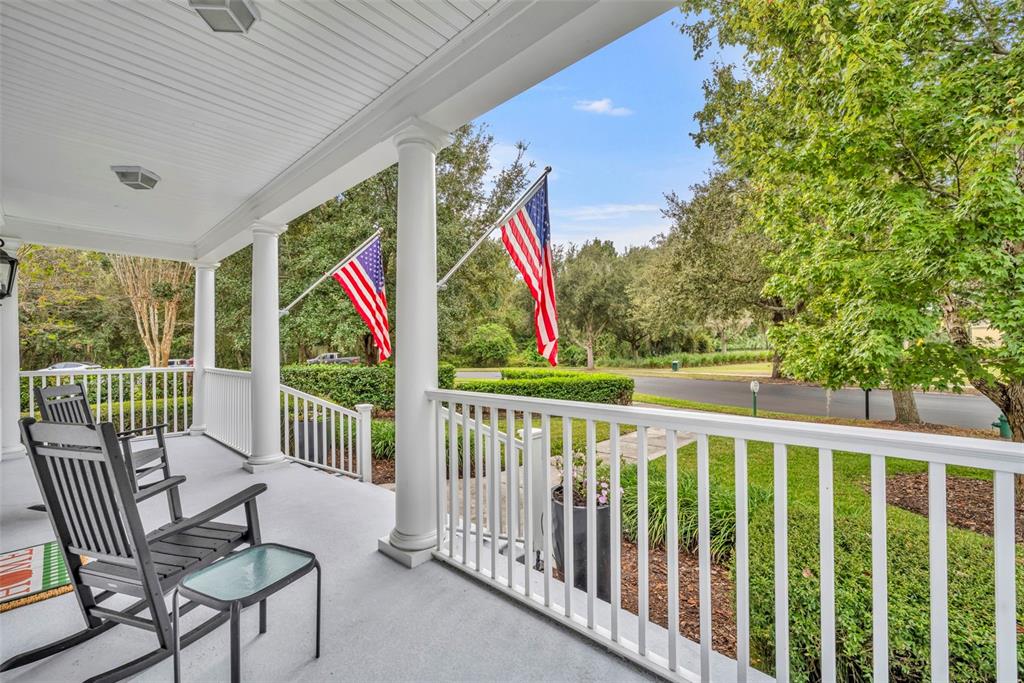 A covered front porch features white railings, columns, rocking chairs, and two American flags — 807 OAK SHADOWS ROAD, CELEBRATION, FL