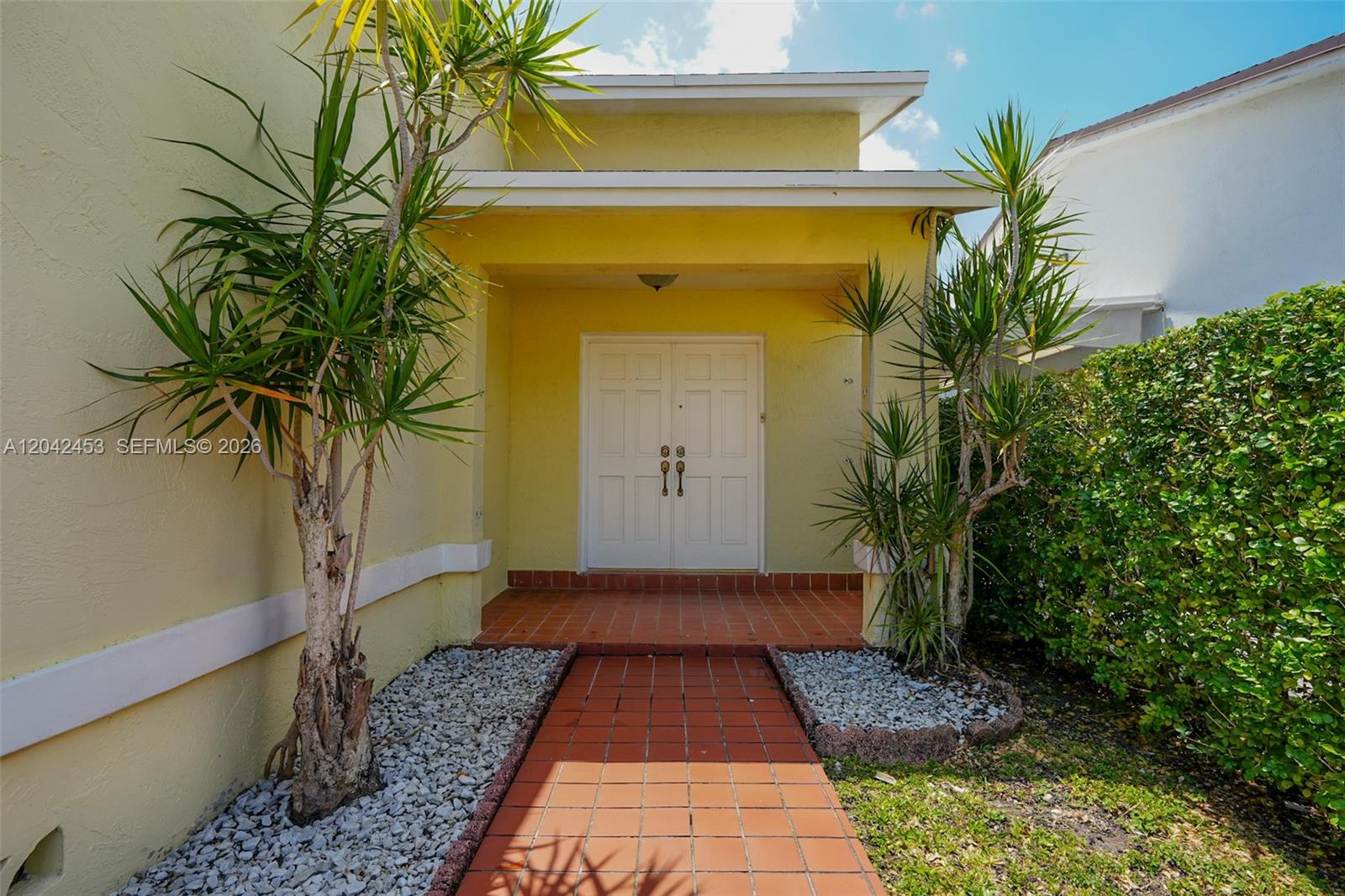 A yellow house exterior features a tiled walkway leading to a double front door — 10920 SW 143rd Ct, Miami FL 33186, MIAMI, FL