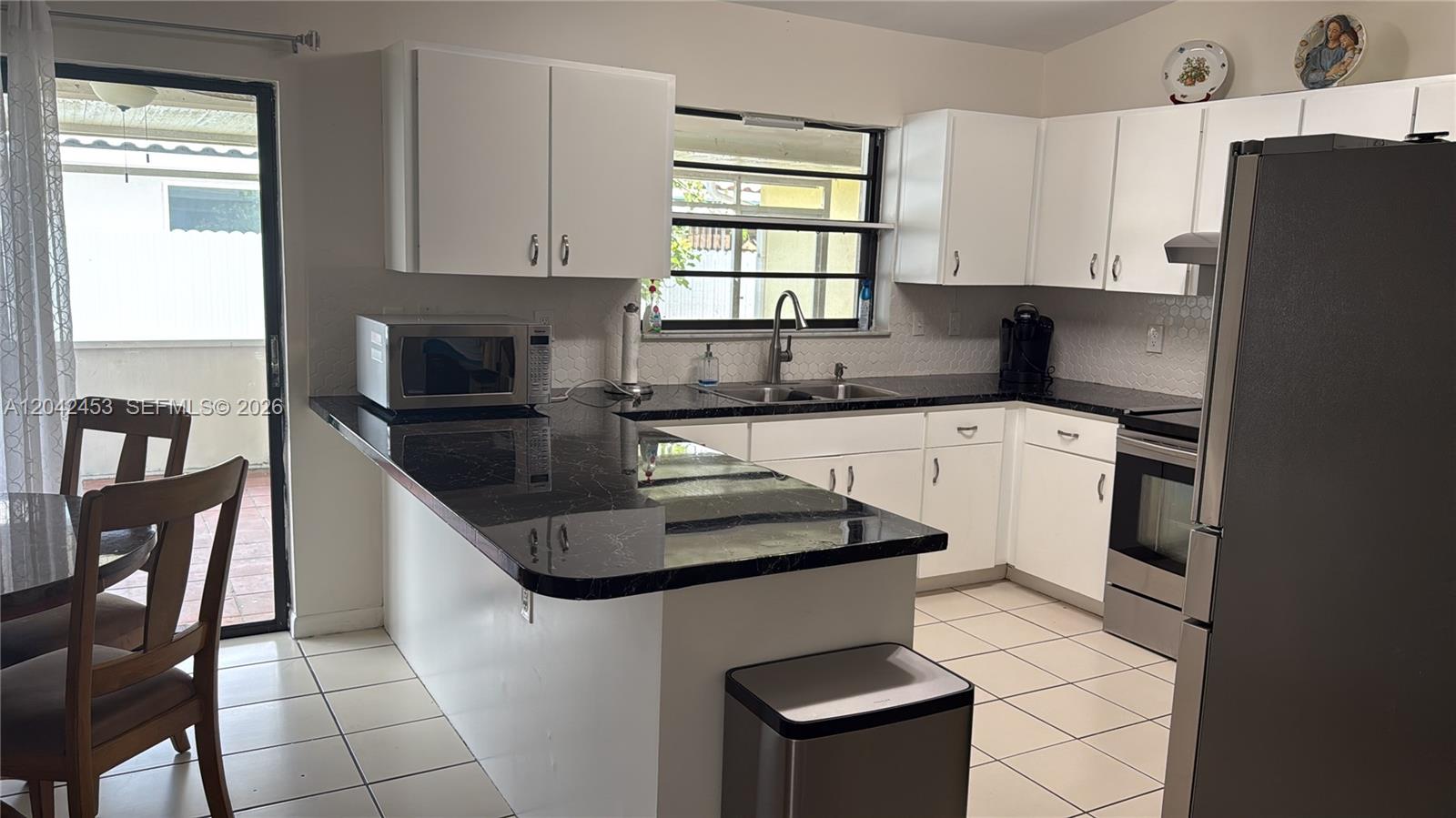 A kitchen features white cabinets, black countertops, stainless steel appliances, and a tiled floor — 10920 SW 143rd Ct, Miami FL 33186, MIAMI, FL