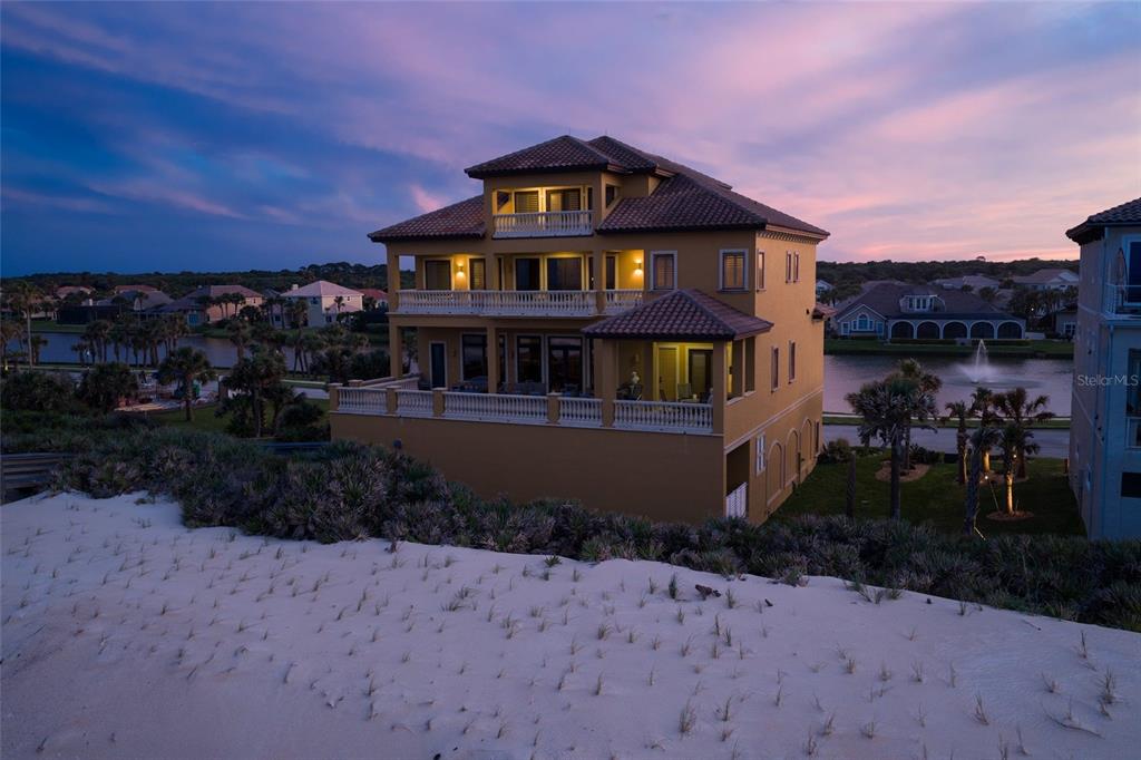 A three-story tan house with multiple balconies sits behind a sand dune at dusk — 35 CALLE DEL SUR, PALM COAST, FL