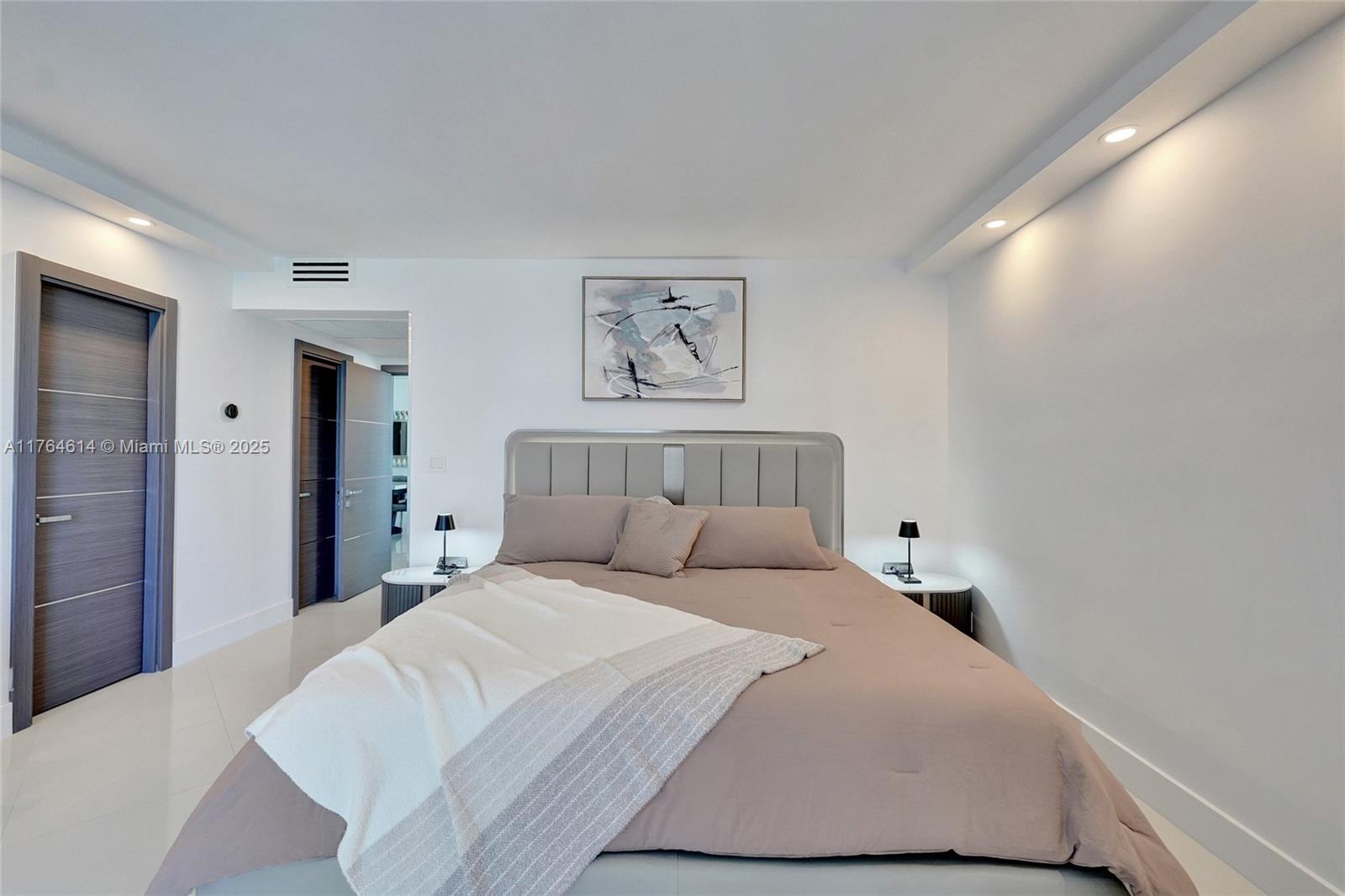 A modern bedroom features a gray upholstered headboard, neutral bedding, and recessed ceiling lighting — 4001 S Ocean Dr # 16P, Hollywood FL 33019, HOLLYWOOD, FL