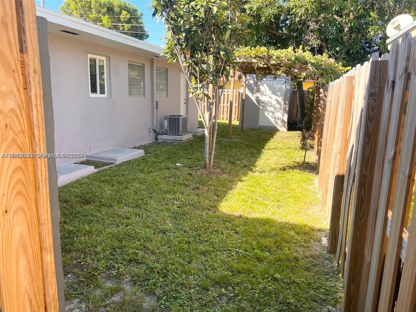 A grassy backyard features a wooden fence, a small shed, and a central tree — 1005 NE 2nd St, Hallandale Beach FL 33009, HALLANDALE BEACH, FL
