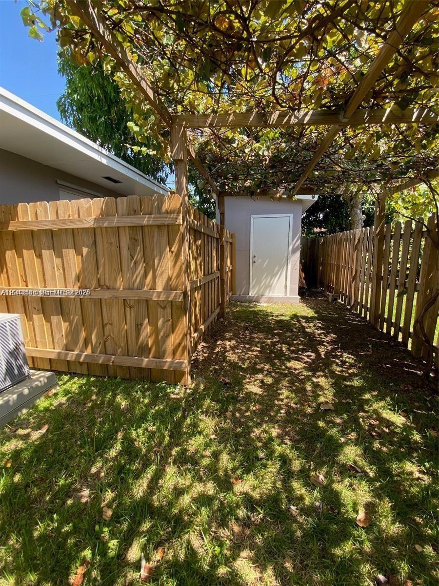 A backyard area features a wooden fence, a small storage shed, and a vine-covered pergola — 1005 NE 2nd St, Hallandale Beach FL 33009, HALLANDALE BEACH, FL